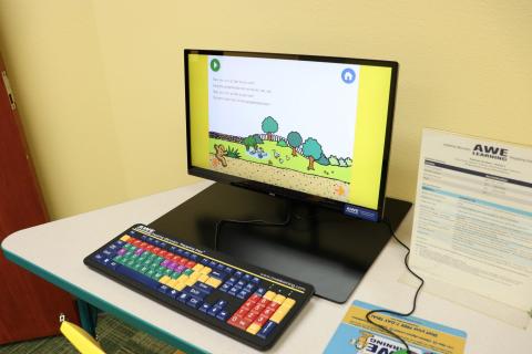 An AWE computer with a colorful keyboard and kid's game on the monitor.