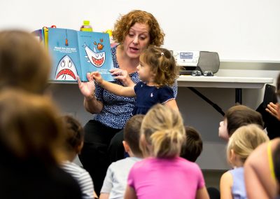 A youth librarian reads a picture book to a group of young children.