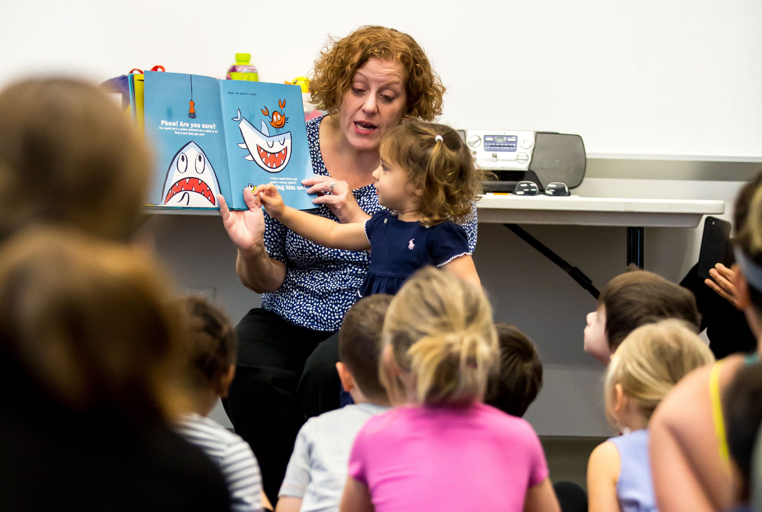 A youth librarian reads a picture book to a group of young children.