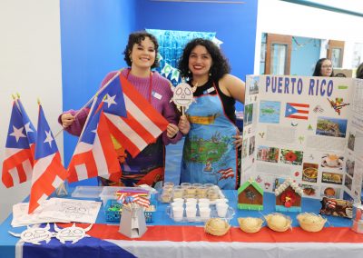 Two members of staff pose in front of a table decorated for the International Festival.