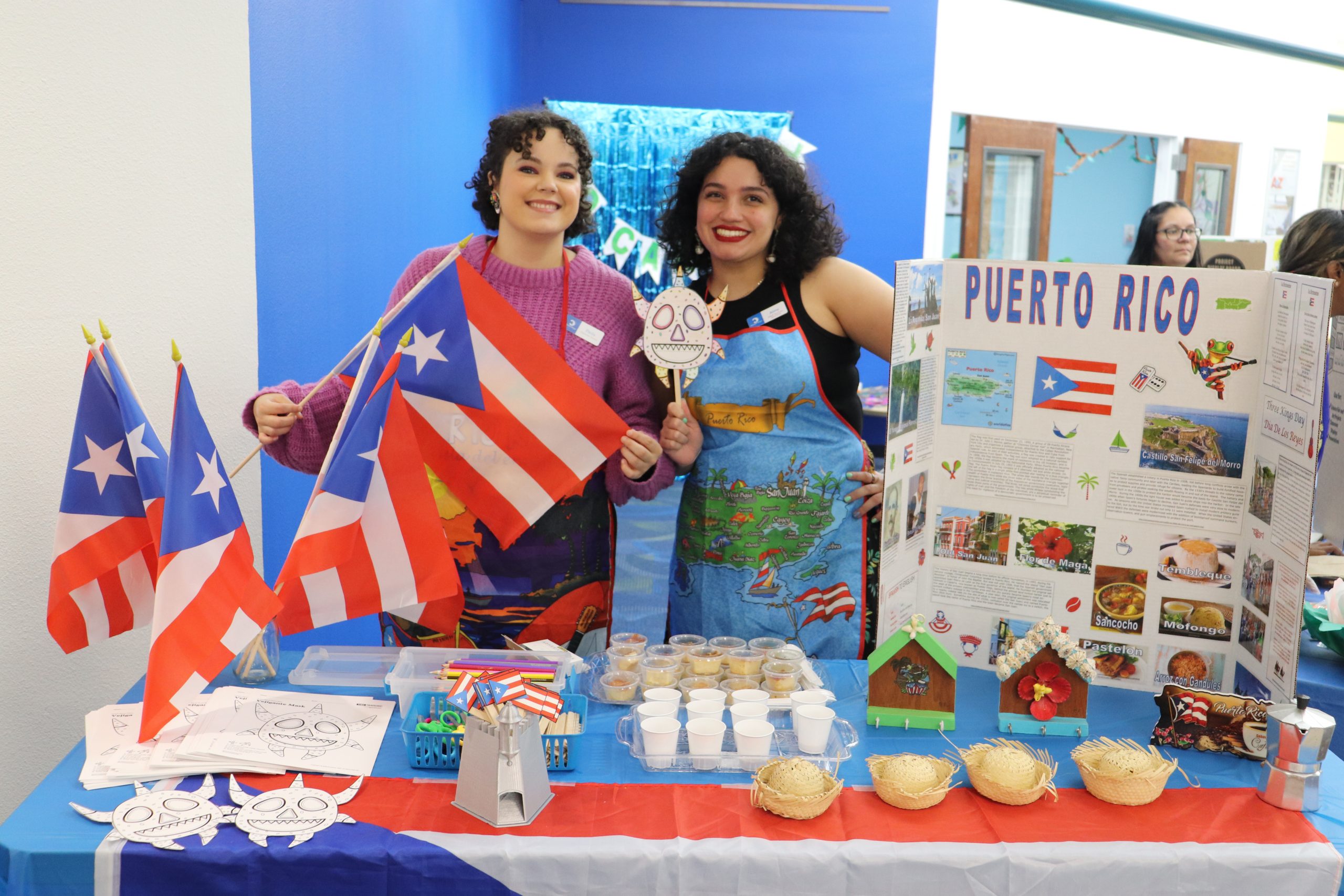 Two members of staff pose in front of a table decorated for the International Festival.